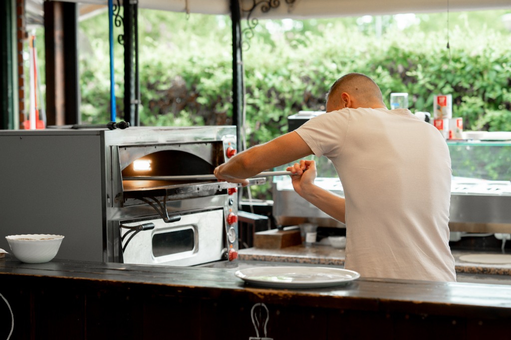 Pizzaiolo lapáttal behelyezi a pizzát a kemencébe
