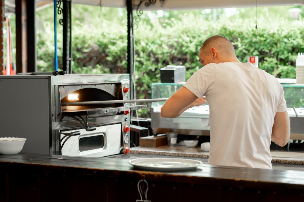 Pizzakészítő kézzel átemeli a feltétezett pizzát a falapátra