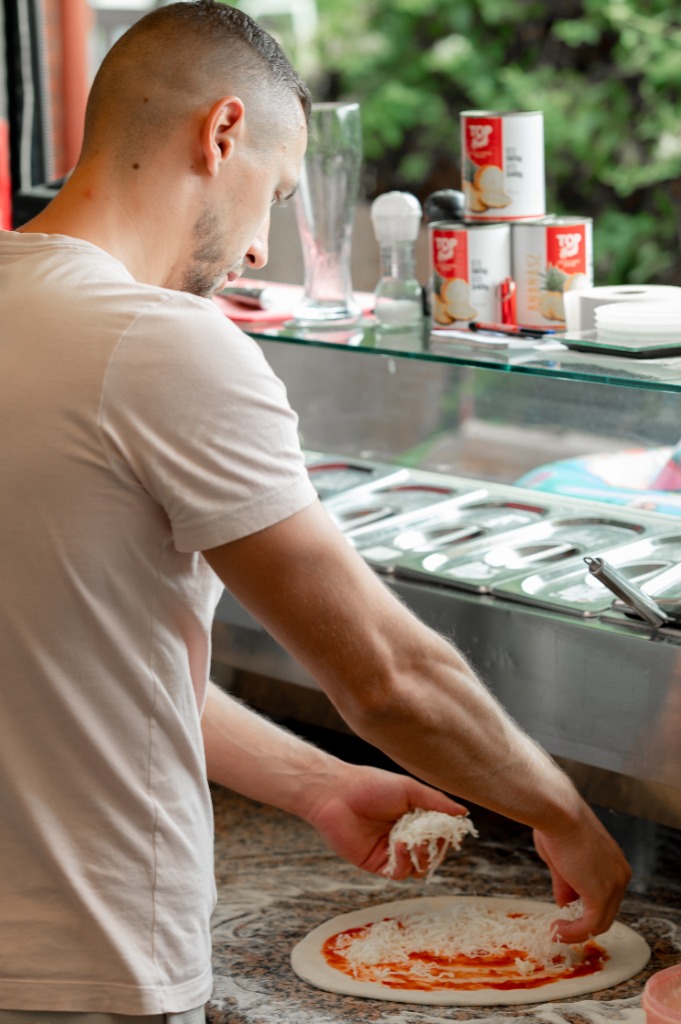 Pizzakészítő igazítja a pizzatésztát a sütőlapáton