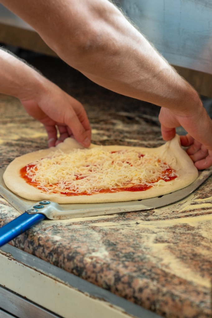 Szakács igazítja a pizza szélét a kemencébe helyezés előtt