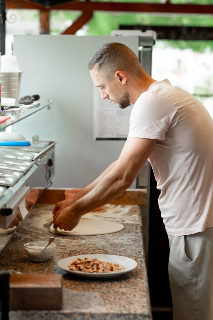 Pizzakészítő lisztezett pulton nyújtja ki a pizzatésztát