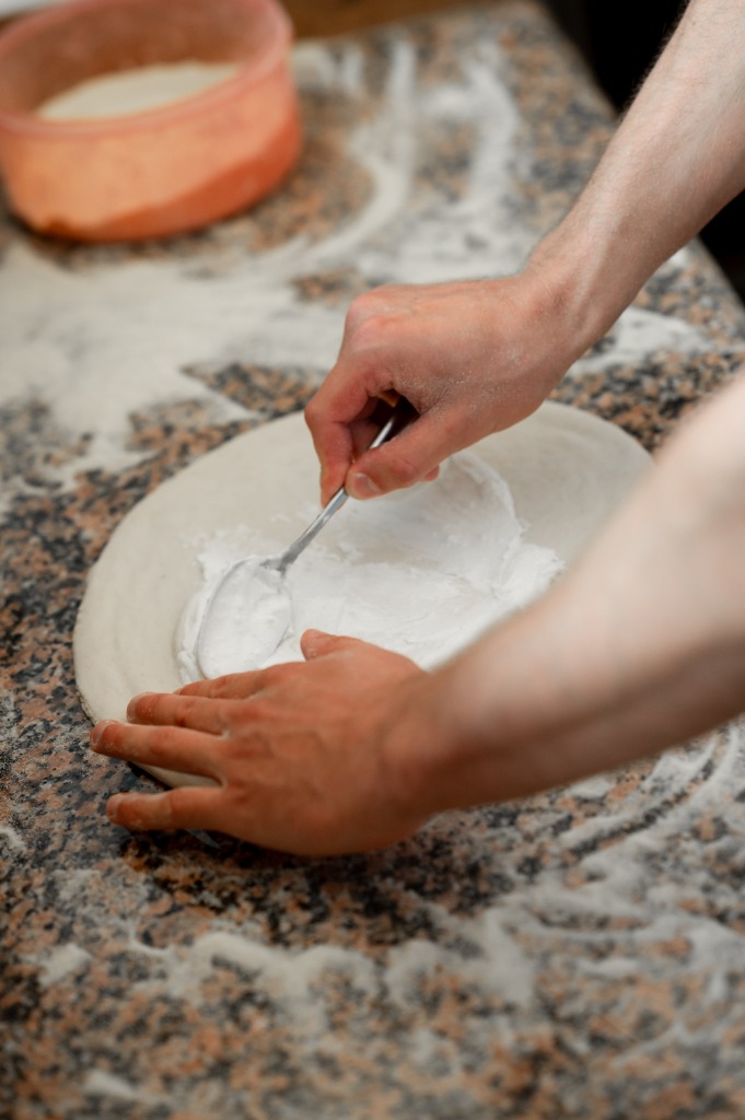 Pizzaszakács kanállal keni szét a tejfölös alapot a tésztán