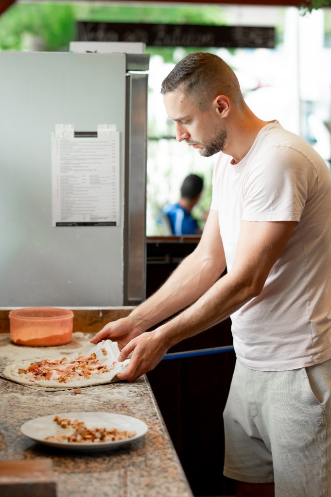 Szakács ráhúzza a feltétezett pizzát a fém sütőlapátra