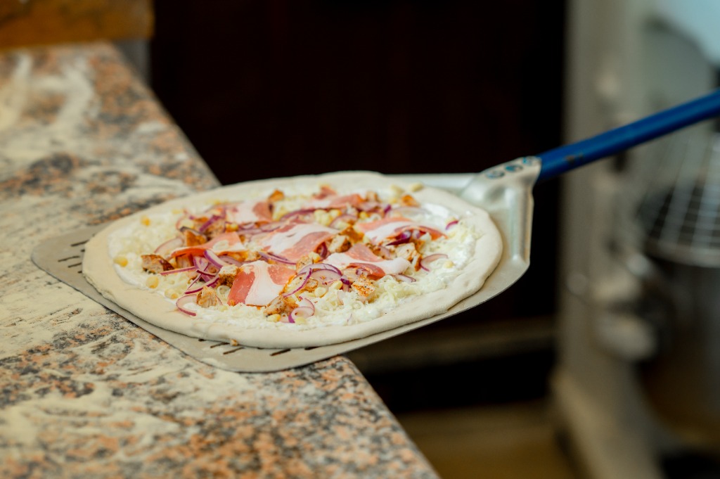 Sütésre kész baconös-hagymás-kukoricás tejfölös pizza a fém lapáton