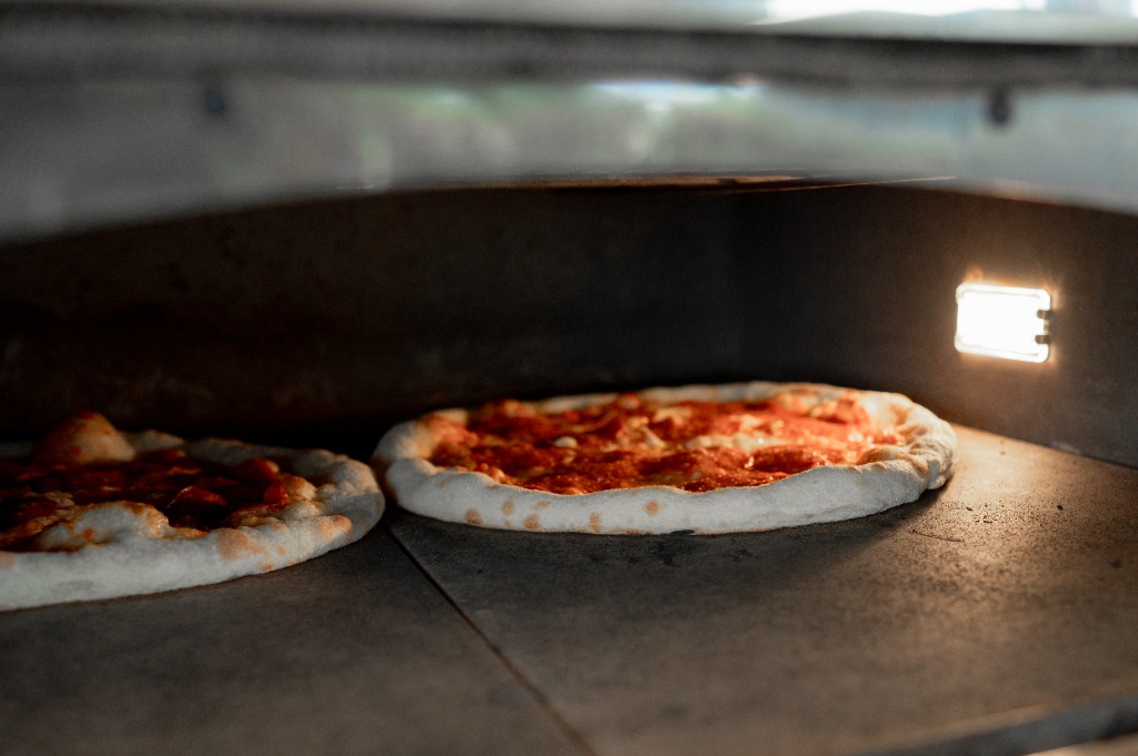 Közelkép a kemencében sülő tejfölös-baconös pizzáról