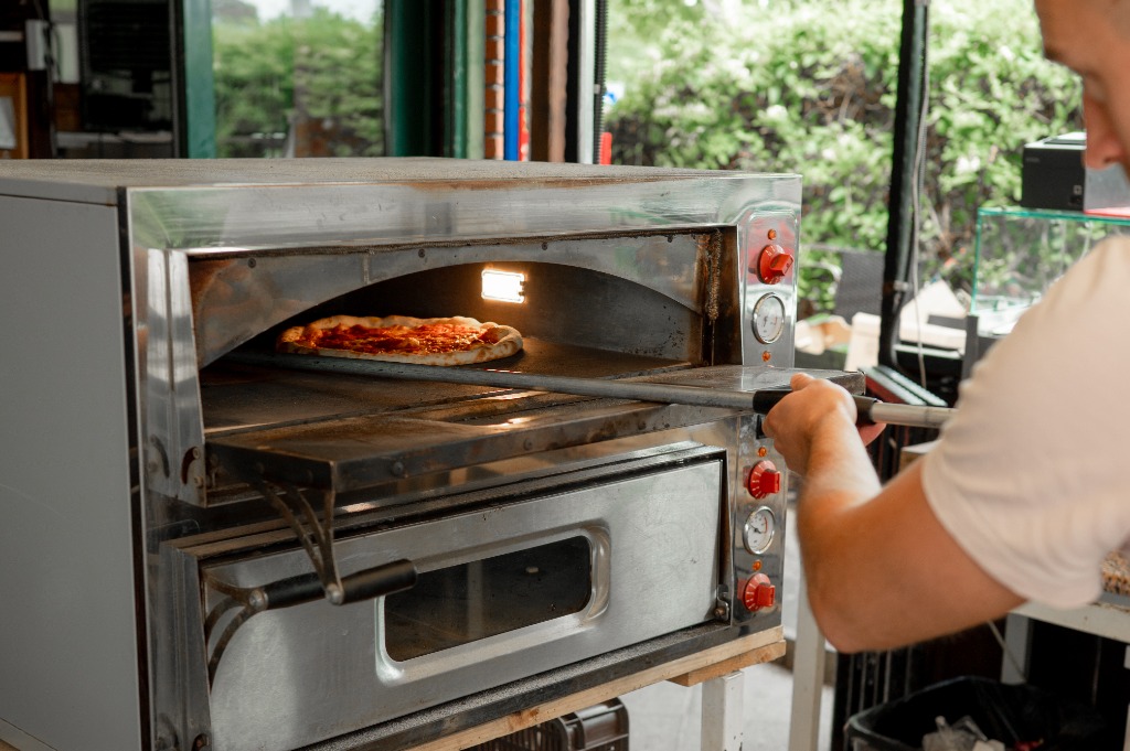 Pizzaszakács a kemence nyílásánál csúsztatja be a pizzát