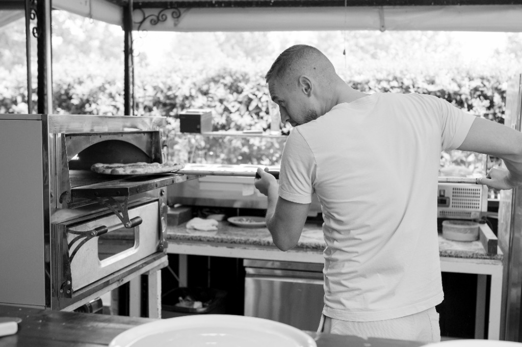 Szakács hosszú fém lapáttal forgatja a pizzát a kemencében