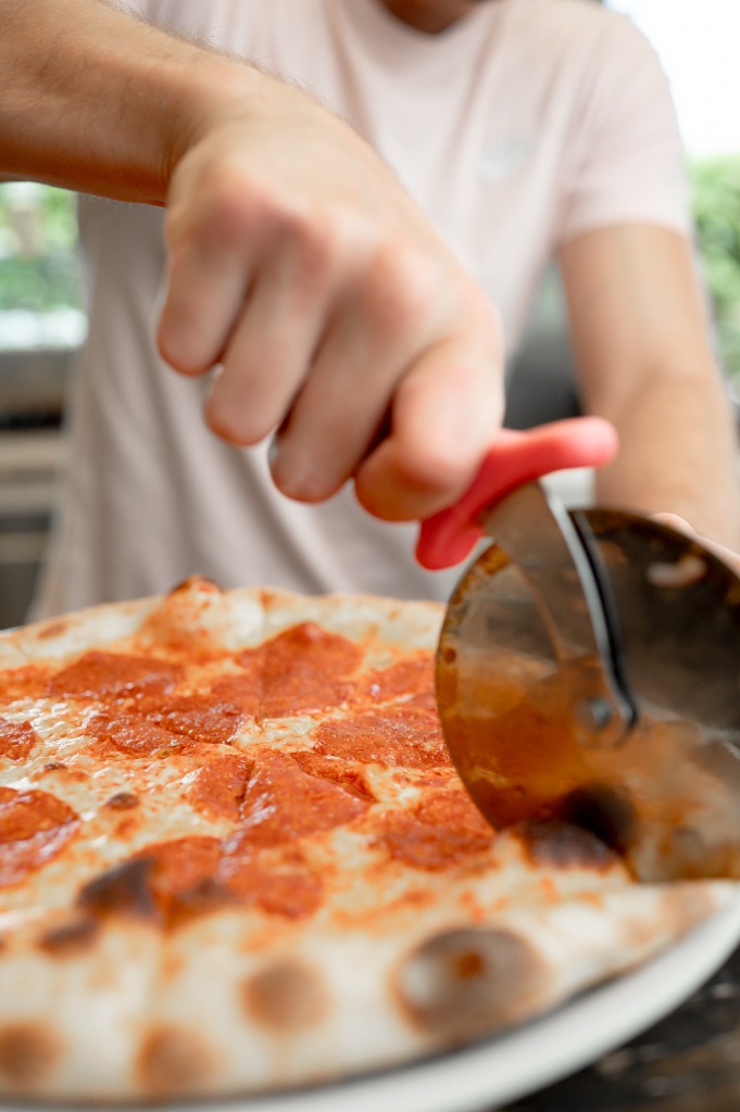 Szakács görgős pizzavágóval szeleteli a friss pizzát