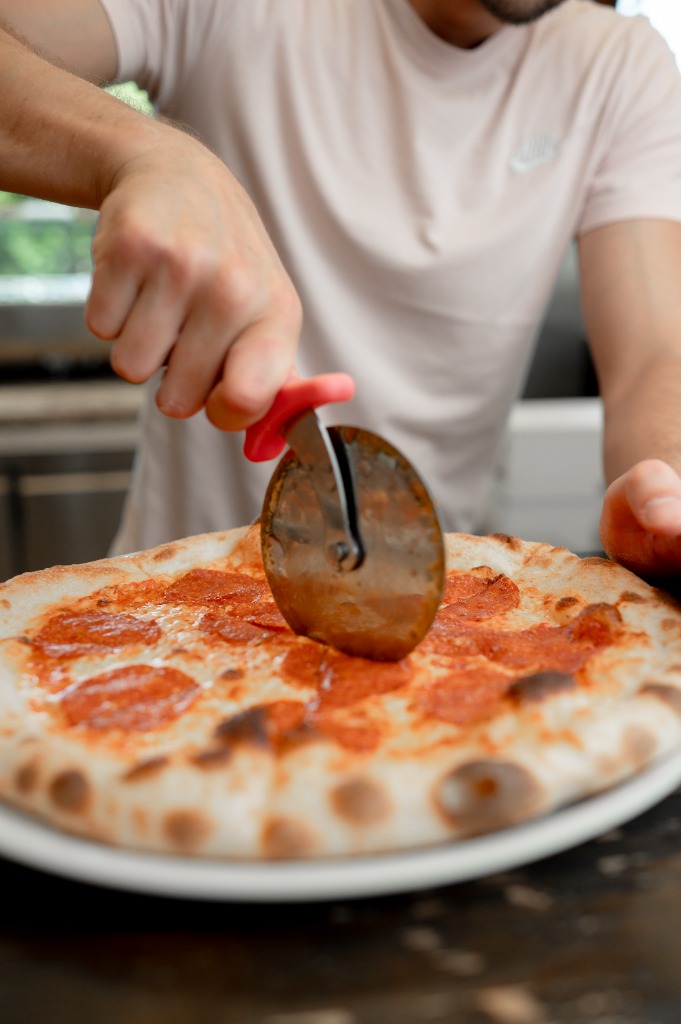 Közeli kép a ropogós szélű pizza szeleteléséről