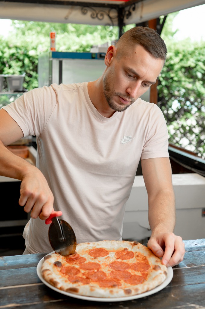 Szakács koncentráltan szeleteli a frissen sült pizzát