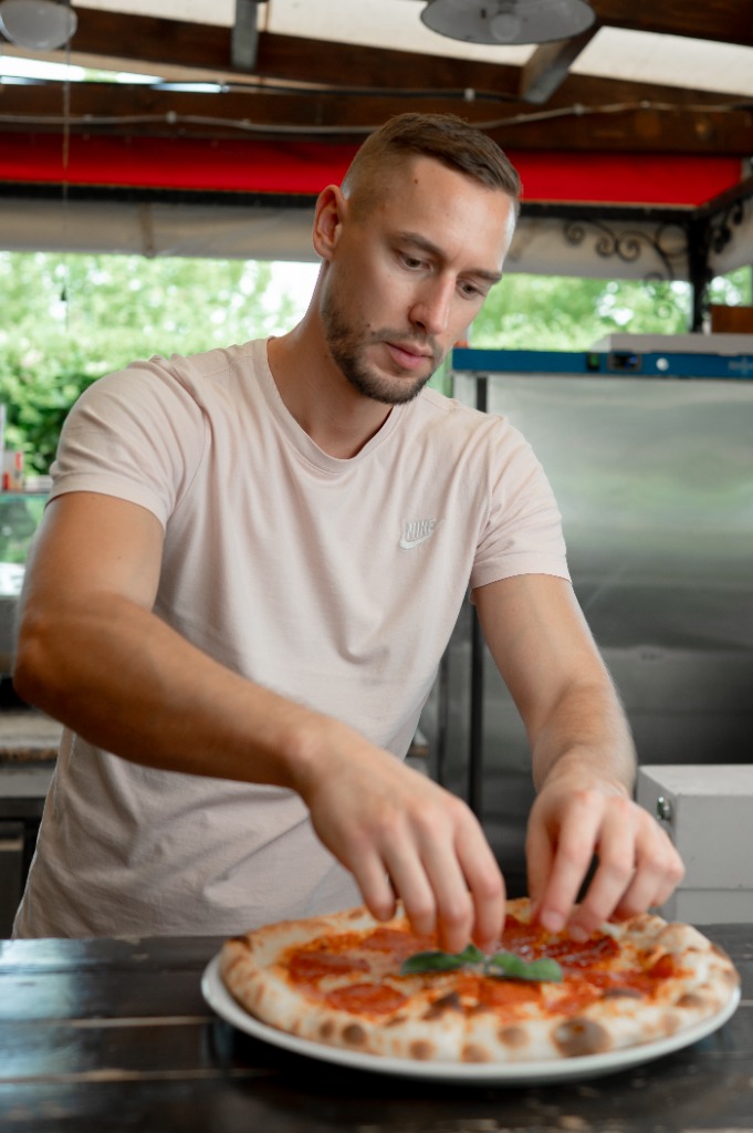 Pizzakészítő friss bazsalikomlevelet helyez a pizza közepére