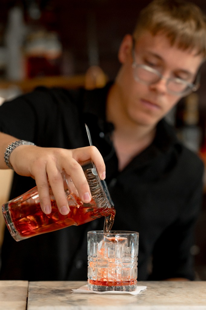 Bártender spirálszűrővel szűri át a Negronit egy whiskys pohárba