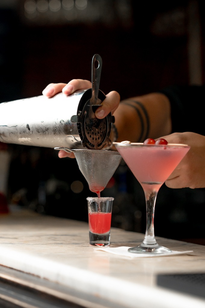 Bártender finomsűrőn keresztül tölti a rózsaszín italt martini pohárba