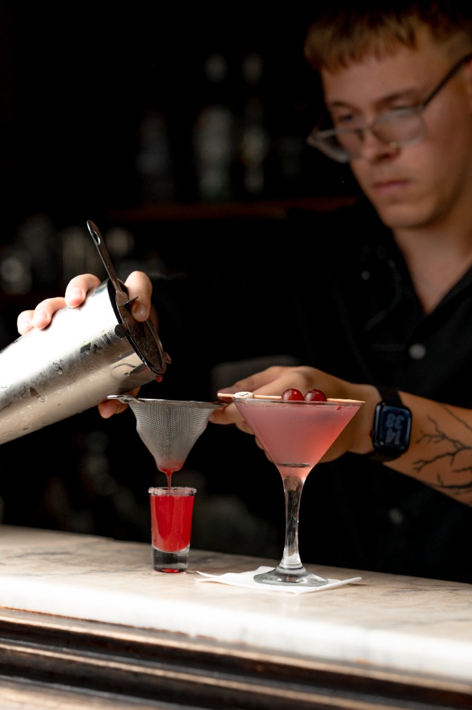 Koktél átszűrése martini pohárba finomszűrővel közelről